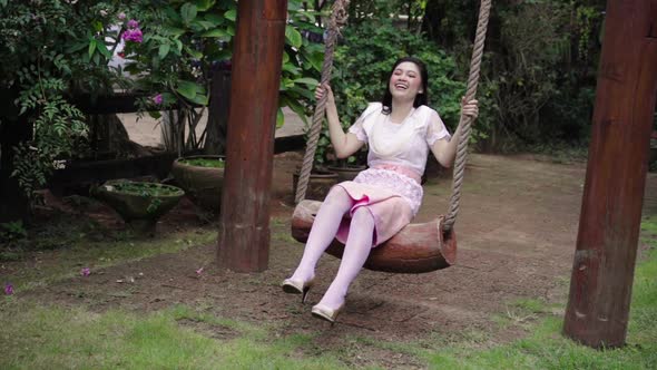 slow-motion of happy young woman in Thai traditional dress relaxing on a wooden swing