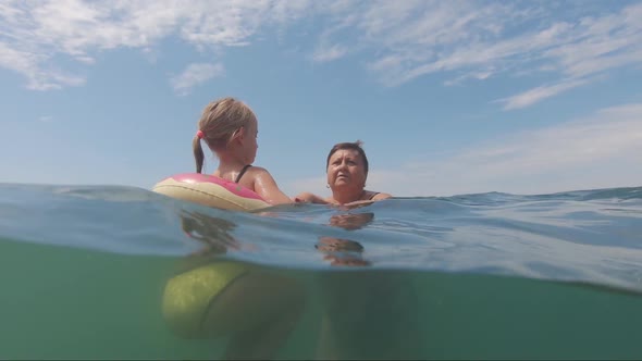 Grandmother with a Small Charming Granddaughter Bathe in the Sea, Happy Family. Grandmother Teaching alt