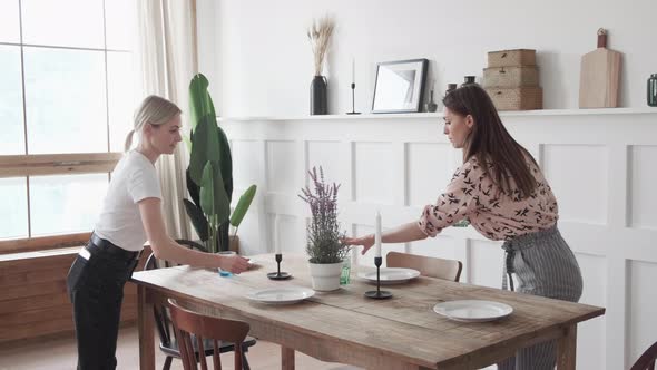 Three girls are smiling standing in the kitchen and laying out plates for a joint dinner alt