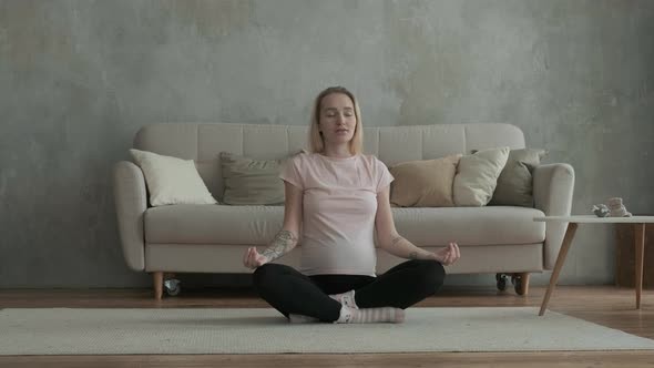 Beautiful pregnant woman is sitting on floor in lotus position