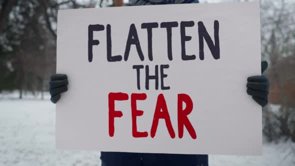 A protester is holding a sign Flatten The Fear. Red and Black writing. Picket. alt