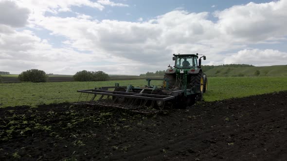 A rural tractor drags a plow across a field with rising dust