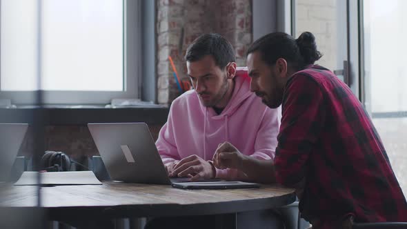 A Young Businessman with a Laptop Talks to a Colleague in the Office alt