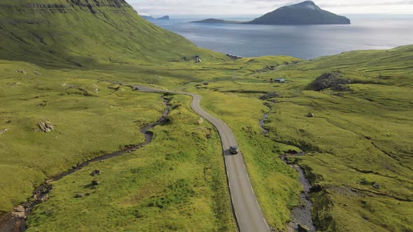 Drone Of Car Driving Along Winding Road In Dramatic Countryside Of Faroe Island alt