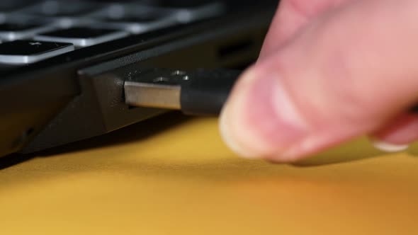 A female hand inserts a USB cable into a laptop. Close-up of USB connector.