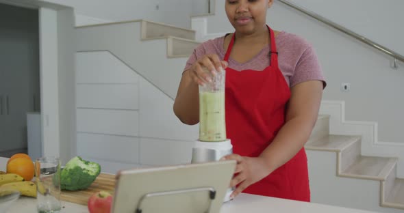 Happy african american plus size woman wearing apron, preparing health drink in kitchen alt