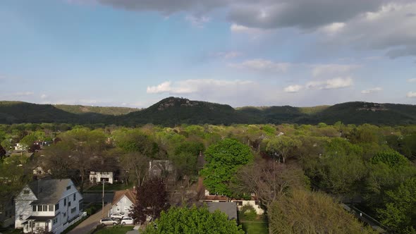 Flyover of midwest town in valley with mountains covered in trees, shadows cast from clouds.