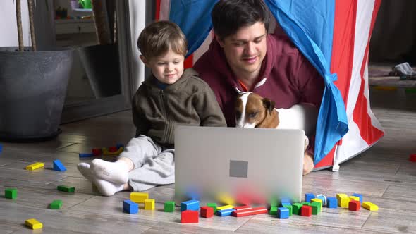 Father and son using laptop computer and lying in a small children's house