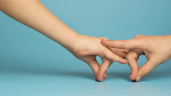 Close up of two child hands playing together isolated on blue background. alt