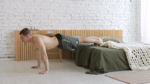 Athletic Young Man Doing Push Ups Exercise with Legs on Bed at Home Side View