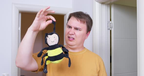 Man Against Background of Doorway Fastidiously Picks Up Soft Toy Bee Old and Dirty