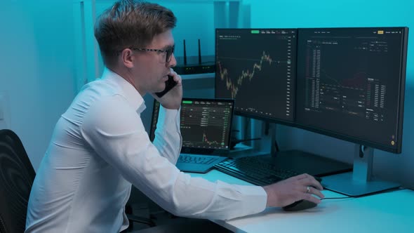 Financial trader working in office filled with computers conducting speaks on the phone alt