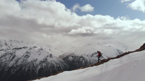 Aerial View Young Man in Sunglasses with a Backpack Goes Down the Mountain on the Crest on the alt