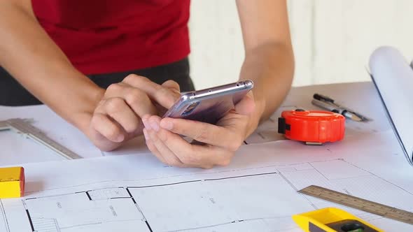 Close up of Architect or Engineer working with cell phone on blueprint. alt