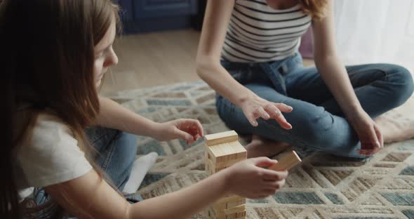 Mother and Daughter Build Tower From Wooden Bricks Sitting on a Floor at Home alt