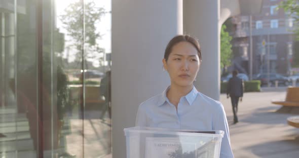 Slider Shot of Asian Sad Businesswoman Walking Outdoors with Box of Stuff Leaving Business Center alt