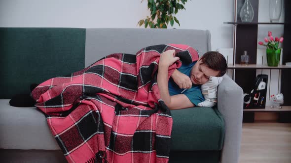 A man lies on the couch, measures his temperature, coughs. Concept of health. alt