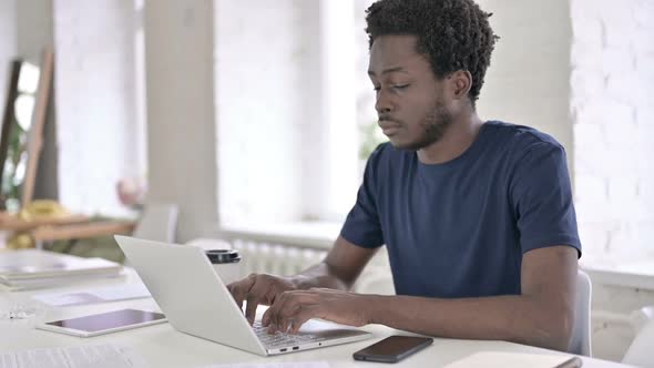 African Man Smiling at Camera While Working on Laptop alt