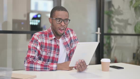 African Man Celebrating Success on Tablet in Office alt