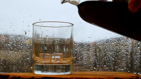 Whiskey On The Bar In The Rain Window. Pour Whiskey At The Bar. A Glass Of Whiskey With Ice alt
