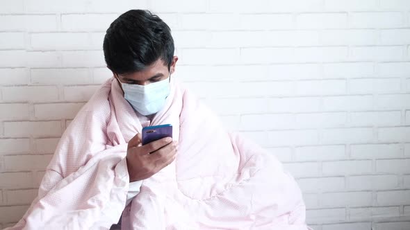 Young Man in Surgical Face Mask Using Smart Phone on Bed alt
