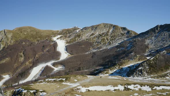 Aerial, Alps Mountains Partially Covered With Snow And Ski Tracks With Artificial Snow In Italy