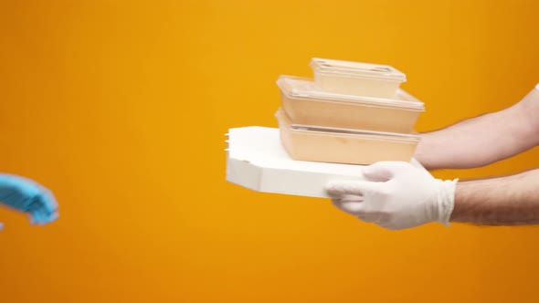 People's Hands Passing Each Other Packed Boxes with Food Delivery Against Yellow Studio Background alt