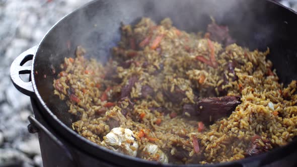 Scooping Up the Finished Uzbek Pilaf with a Slotted Spoon From a Cauldron alt