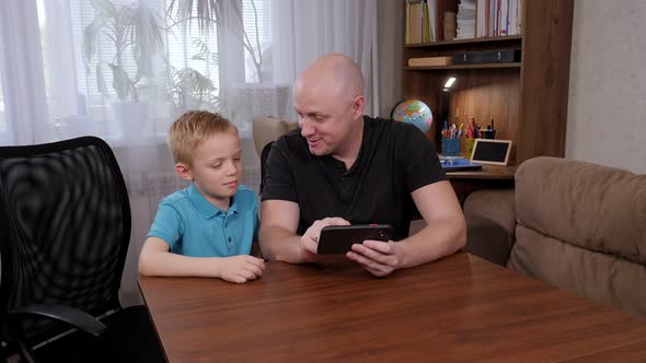 Portrait of a Father with His Son at Home with a Phone in Their Hand alt