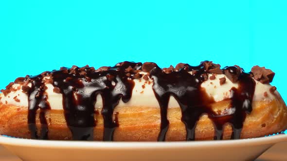 Sweet Eclair with Chocolate Sprinkles Rotating on a Wooden Table on a Blue Background alt