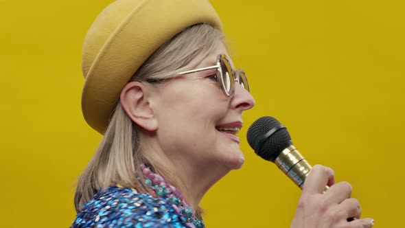 Portrait Of An Elderly Woman On Yellow Background With Microphone In His Hands alt