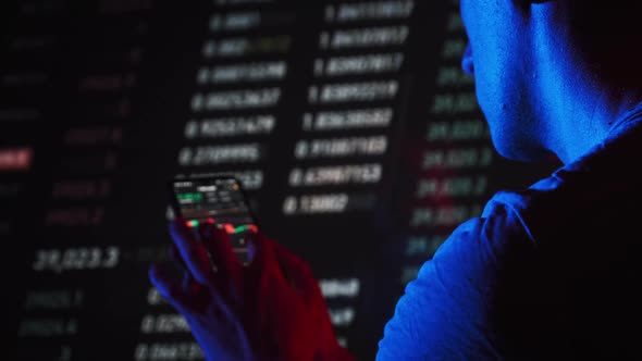 Trader Analyzes Cryptocurrency Charts on a Smartphone Screen in the Dark alt