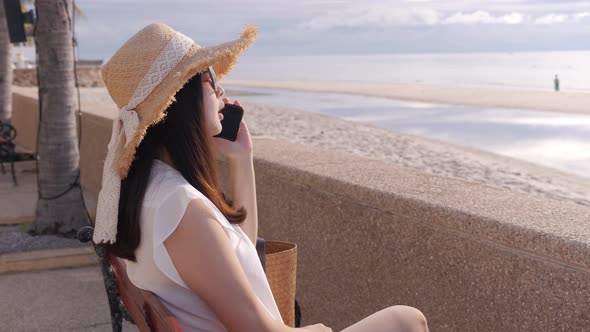 Side view, close up of Asian woman using mobile phone, sitting on beach bench alt