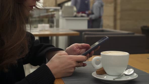 Handheld Shot of Woman Typing on the Phone Drinking a Cup of Coffee
