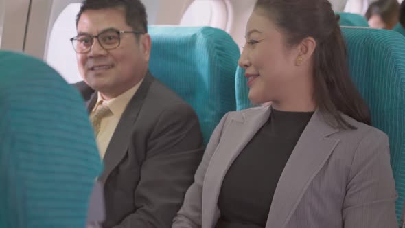 Happy Asian businessman and businesswoman sitting at seat on airplane cabin alt