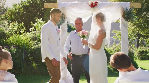 Caucasian bride and groom standing at outdoor altar with wedding officiant during ceremony alt