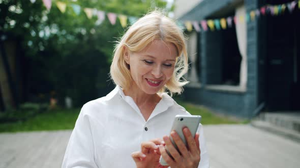 Joyful Woman Using Smartphone Looking at Screen Smiling Standing Outdoors alt