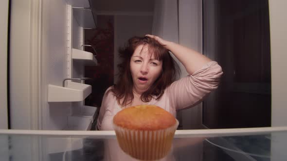 Sleepy Woman Takes a Cupcake From the Fridge at Night