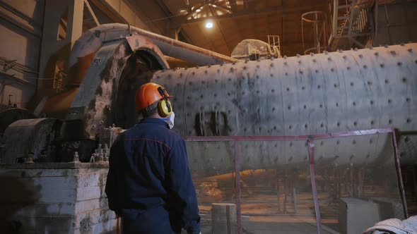Worker in the workshop at factory with metal works. A worker wears protective helmet and headphones alt