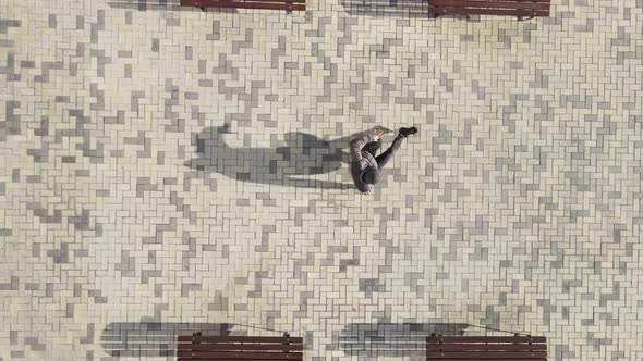 A Dancer in a Hood Dances Breakdancing on a Street Tile alt