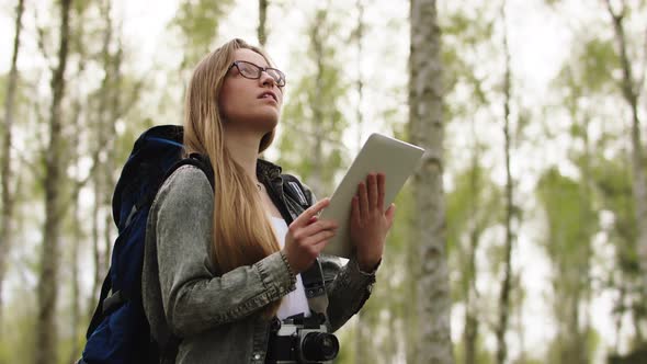 Young Caucasian Woman Backpacker Using Tablet for the Orientation in the Forest. Low Angle Shot alt