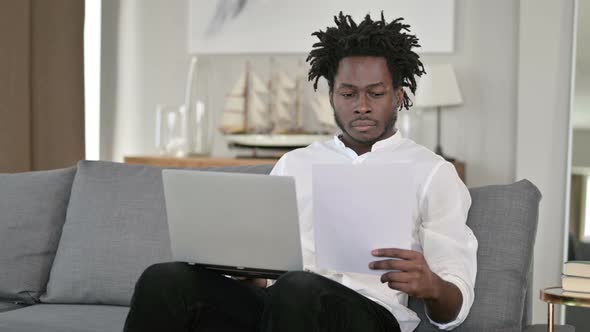 African Man Working on Documents and Laptop at Home  alt