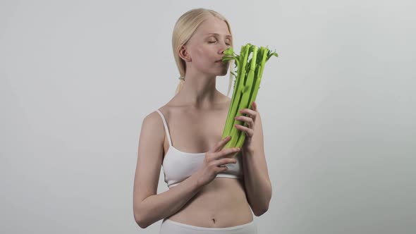A Joyful Woman with a Beautiful Slender Body in Underwear Holds Fresh Celery in Her Hands
