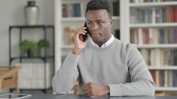 African Man Talking on Smartphone in Library alt