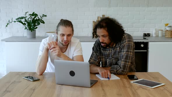 Two Young Freelance Guys Work Remotely At Home on an Online Project, Using a Laptop and a Tablet alt