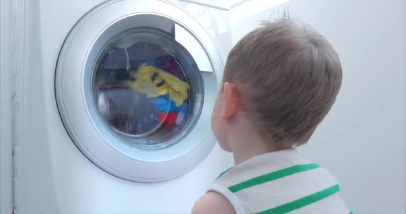 Cute Child Looks Inside the Washing Machine. Cylinder Spinning Machine. Concept Laundry Washing alt