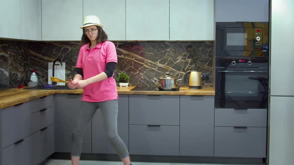 Girl in a Hat and Bright Pink Tshirt Has Fun and Dances in the Kitchen While Cooking