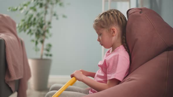 Upset Girl with Gymnastic Hoop Sits in Bean Chair at Home alt