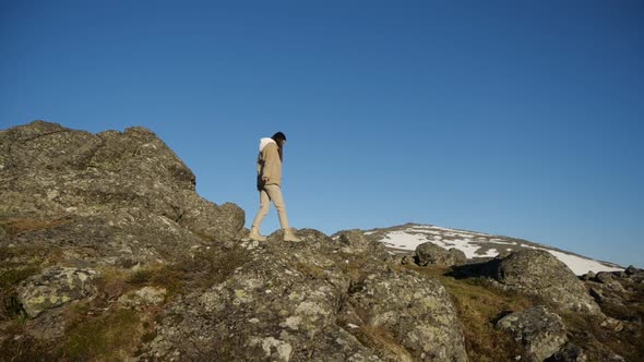 A Girl Walks on the Edge of a Cliff Against the Background of Mountain Peaks