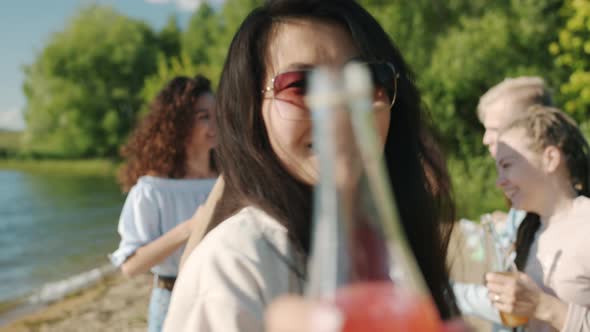 Portrait of Happy Asian Girl Wearing Sunglasses Dancing on Beach Holding Bottle with Drink alt